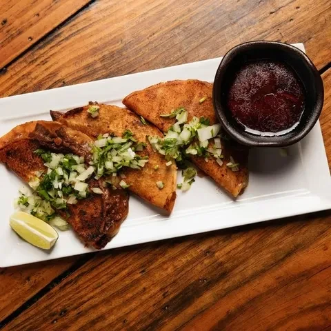 Golden fried tacos garnished with onion, cilantro, lime, and sauce.