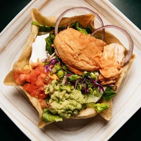 Colorful chicken taco salad in a crispy tortilla bowl with guacamole.