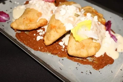 Three fried pastries with white sauce, red sauce, cheese, and flower garnish.