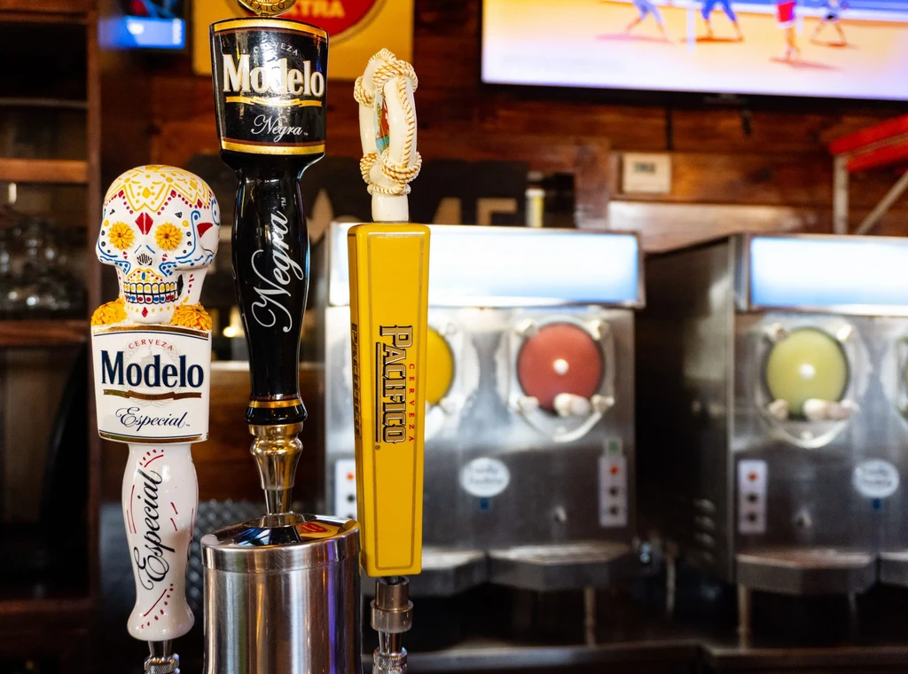 Three distinct Modelo and Pacifico beer tap handles at a bar.