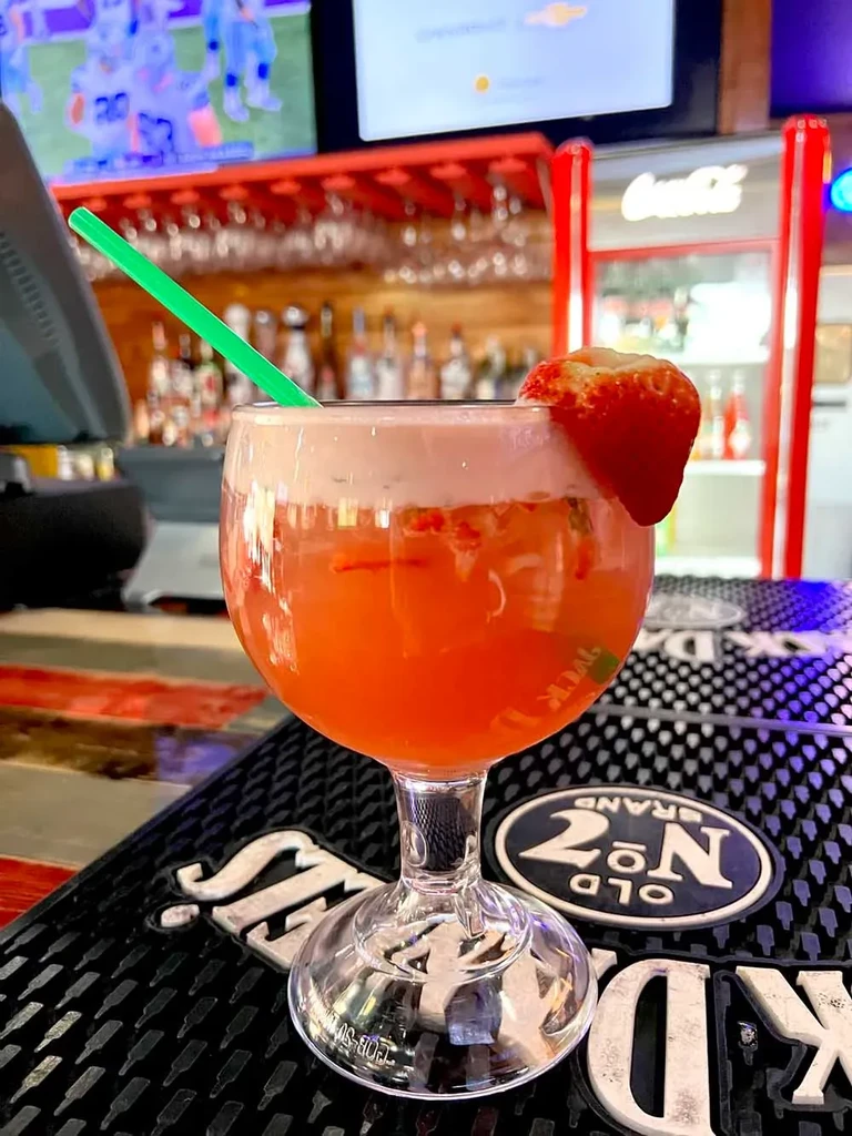 Orange cocktail with strawberry, green straw, on branded bar mat.