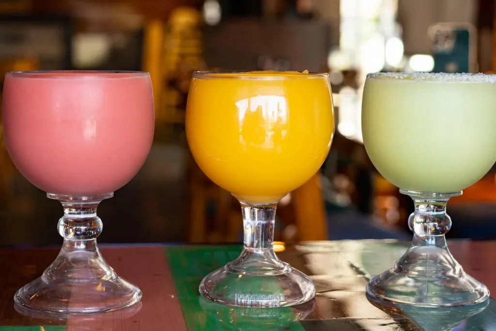 Three stemmed glasses with pink, yellow, and green drinks, one rim-coated.