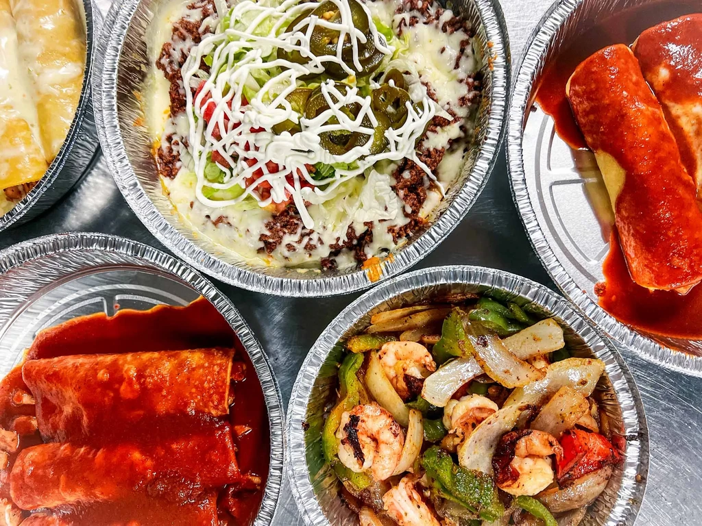 Overhead: assorted takeout meals in foil containers on metal.