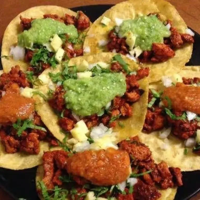 Six al pastor tacos with various salsas and toppings on a dark plate.