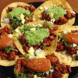 Close-up of several tacos with red meat, green salsa, onion, cilantro.