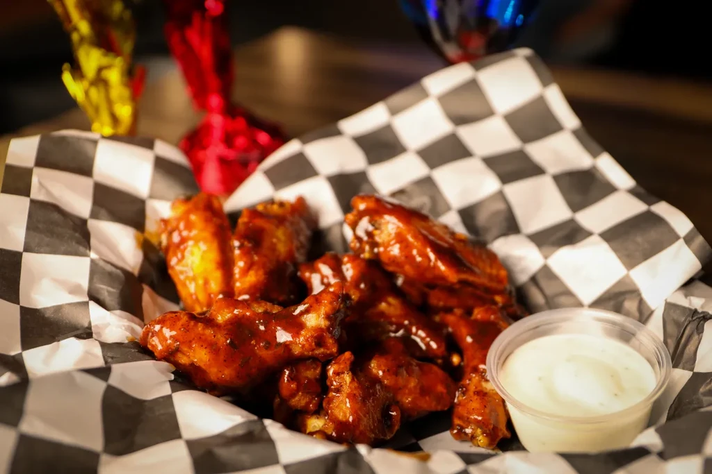 Basket of dark, glossy chicken wings and a creamy dipping sauce.