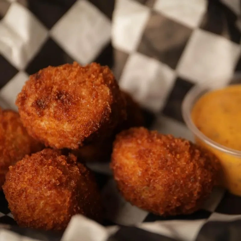 Crispy golden-brown fried food in a checkered container with dipping sauce.