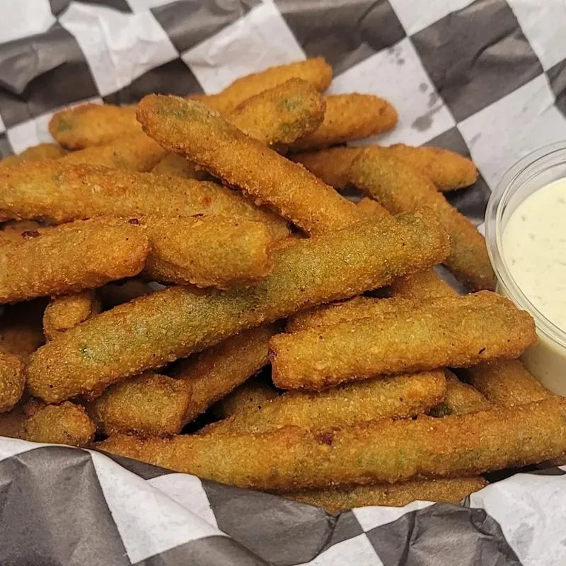Basket of golden-brown fried pickles or okra with dipping sauce.