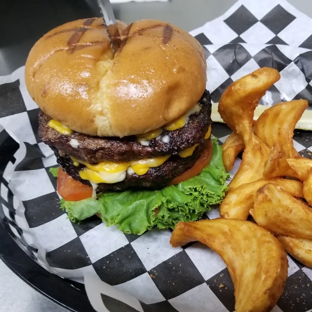 A double cheeseburger with melted cheese, lettuce, tomato, and wedge fries.