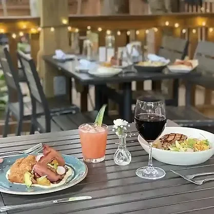 Outdoor evening table with various dishes, cocktails, wine, and string lights.