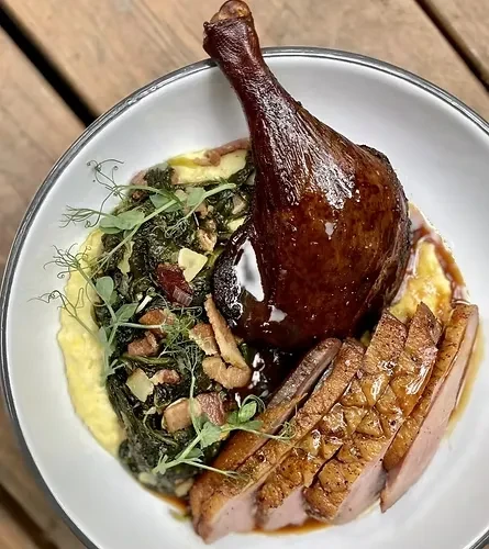 Upright duck leg, sliced breast, vegetables, purée, sauce, and microgreens.