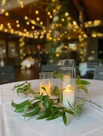 Table centerpiece with lit candles, greenery, and warm blurred background lights.