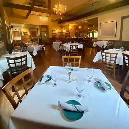 Warm, upscale restaurant interior with elegantly set tables and chandeliers.
