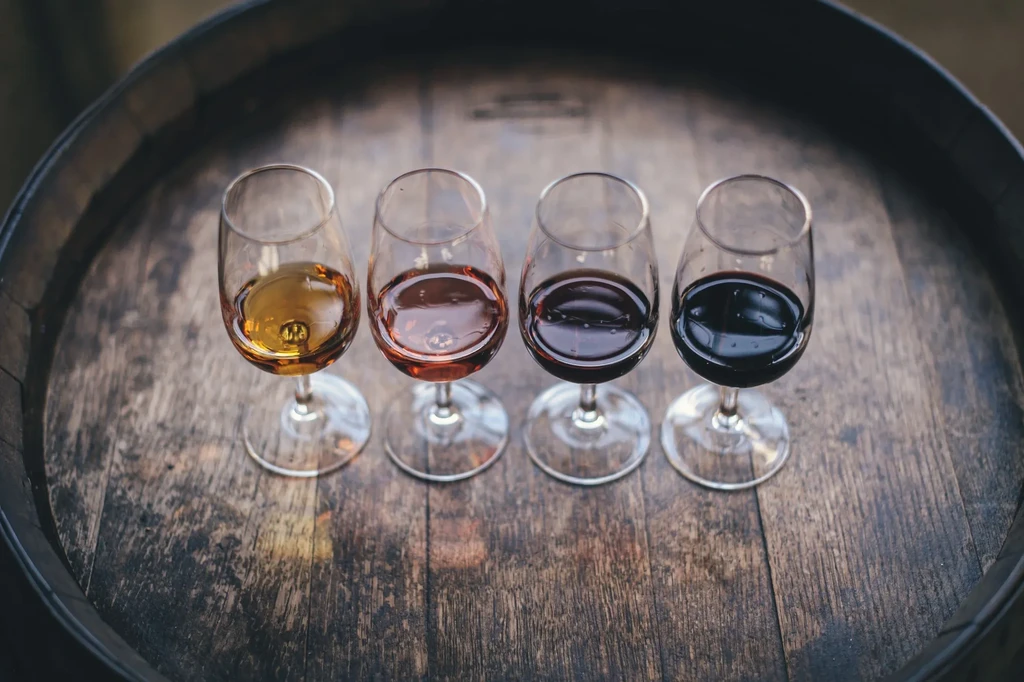 Four stemmed glasses with a gradient tasting flight on a wooden barrel.