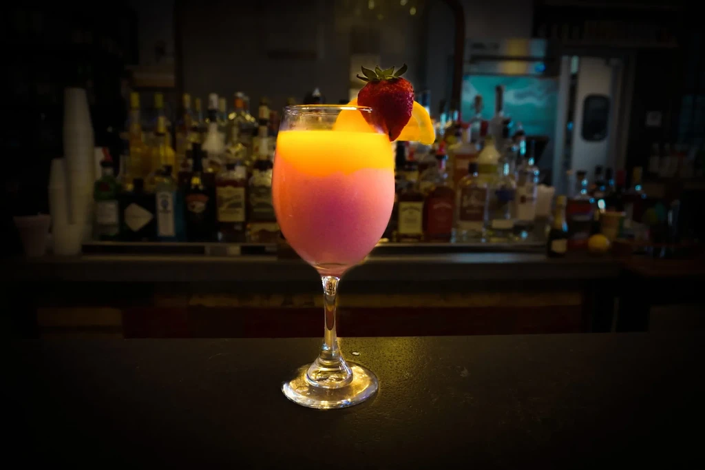 Layered orange and purple cocktail with strawberry, citrus on a bar.