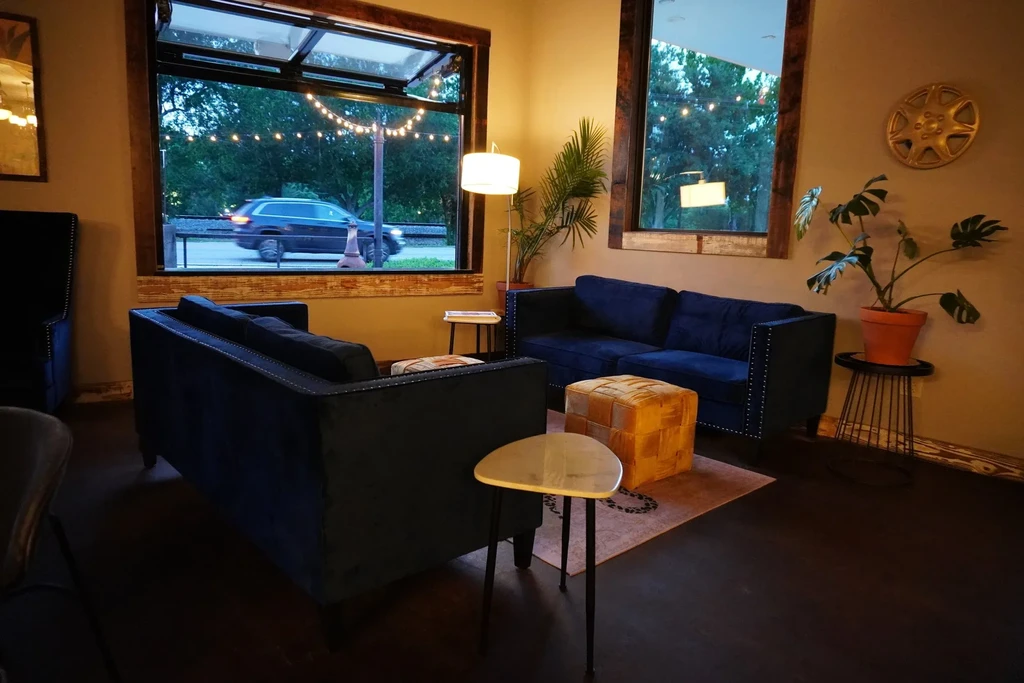 Cozy seating with blue sofas, brown pouf, plants, and an evening street view.