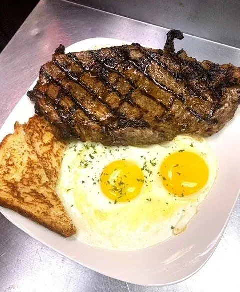 Grilled steak, two sunny-side-up eggs, and toast on a white plate.