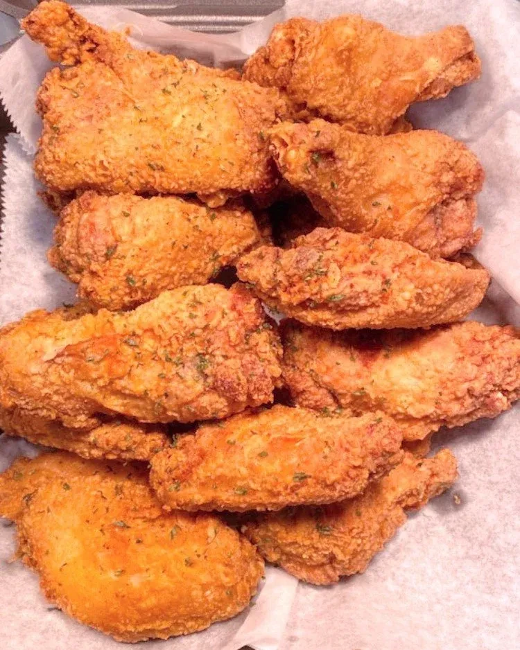 Close-up of crispy, herb-seasoned fried chicken in a take-out container.