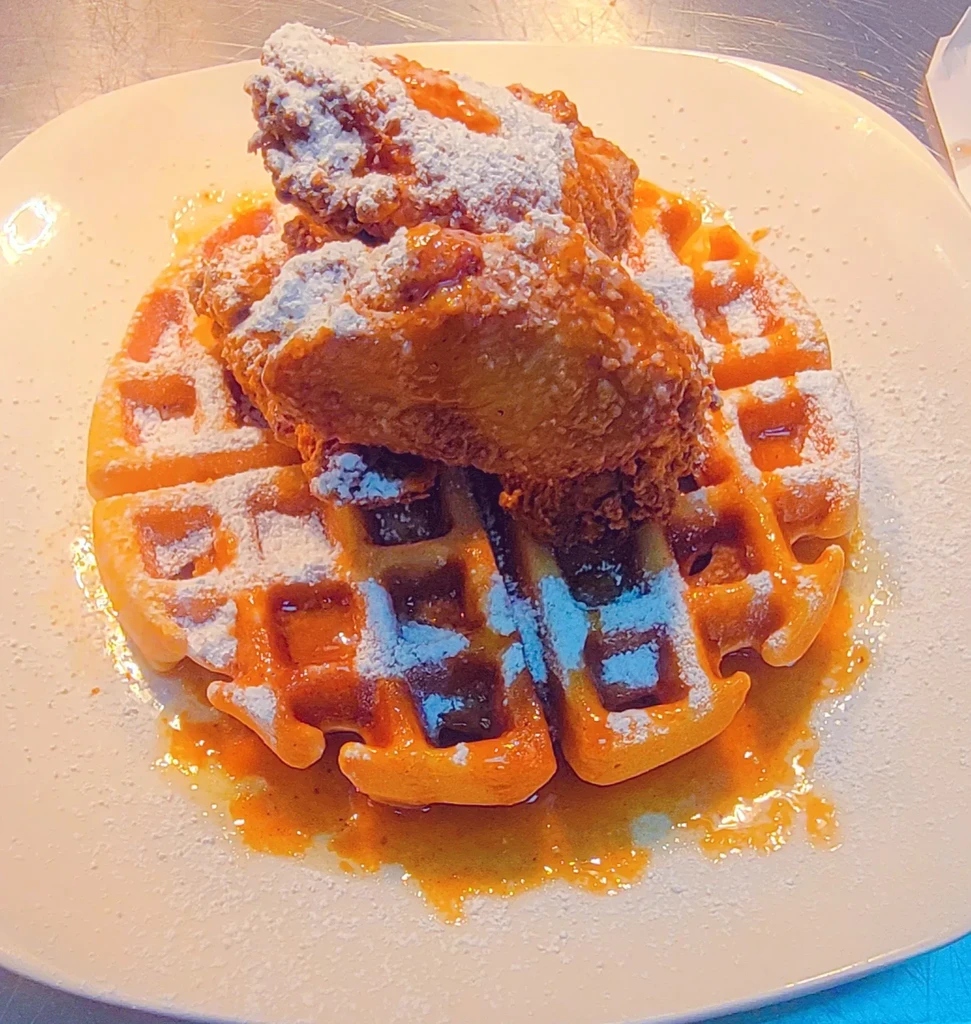 Crispy chicken and waffles topped with powdered sugar and syrup.