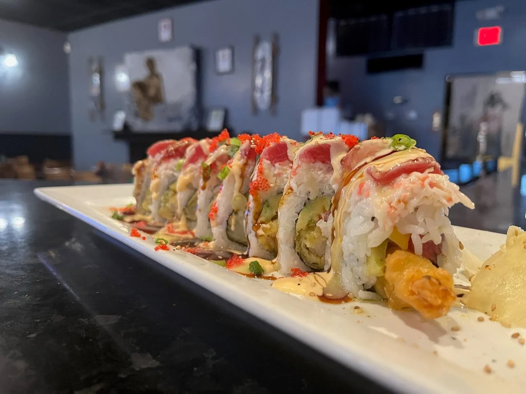 Platter of tuna and tempura sushi rolls with roe and sauces.