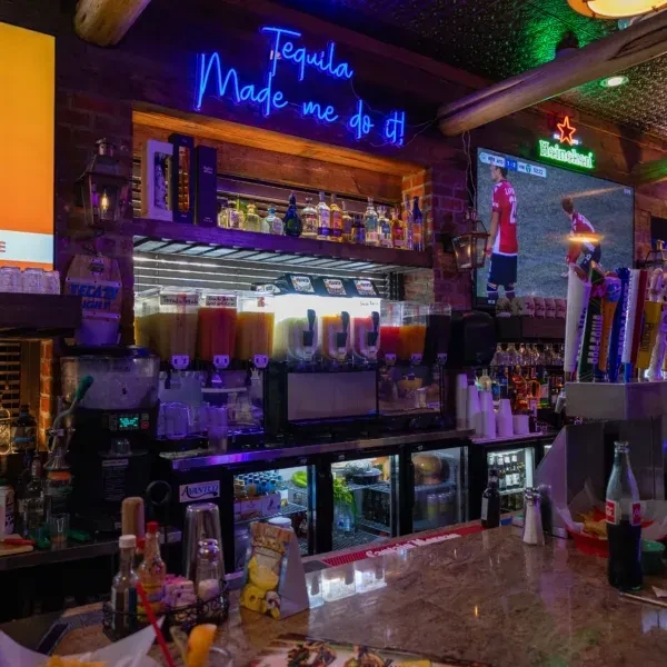 A well-stocked bar with frozen drinks, liquor, beer taps, and a neon sign.