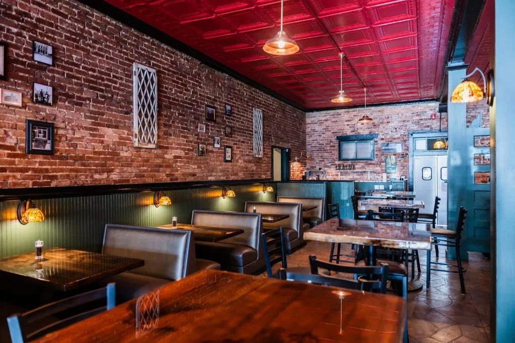Empty rustic restaurant interior featuring brick walls, tin ceiling, and warm lighting.