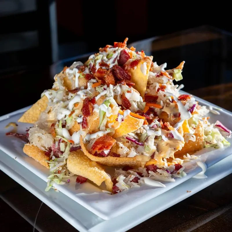 Loaded fried wonton nachos with bacon, cabbage, and creamy white sauce.