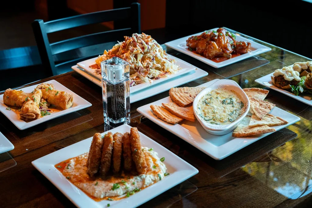 Multiple plates of appetizers: nachos, wings, rolls, dip, and fried shrimp.