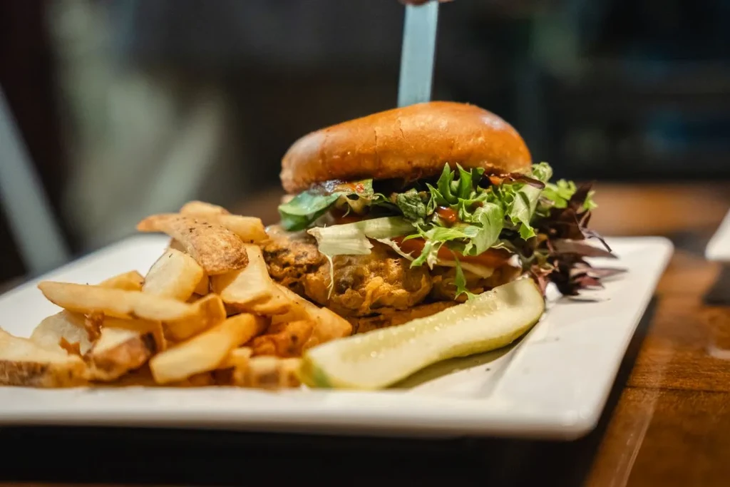 Burger with knife, potato wedges, and pickle on a rectangular plate.