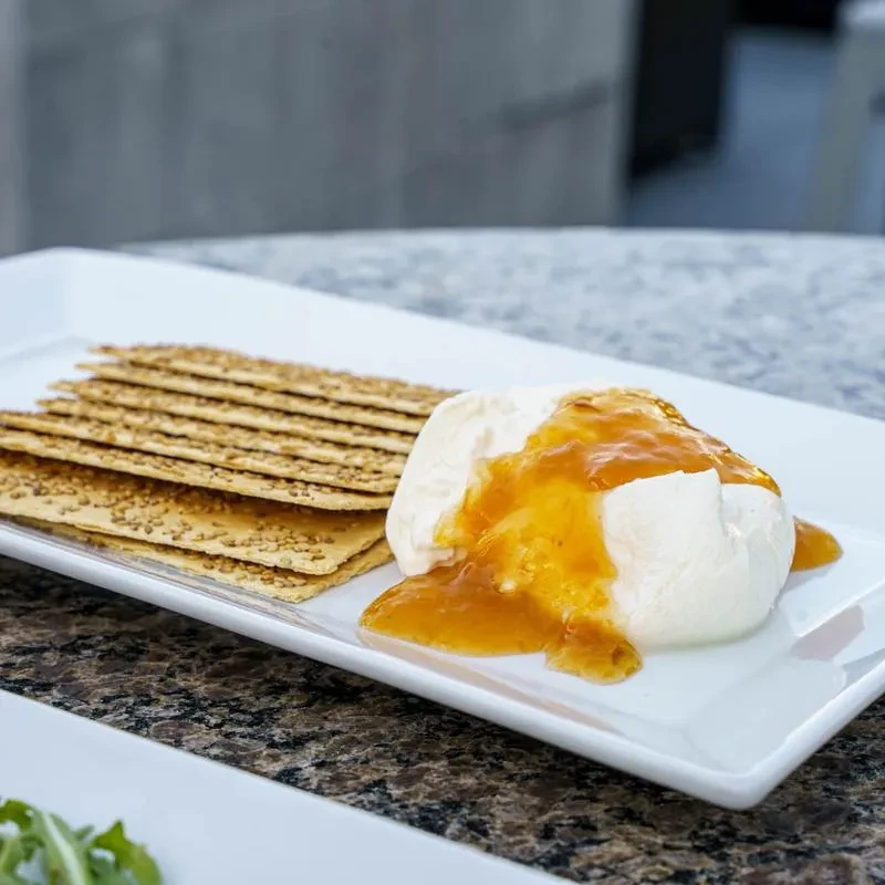 Burrata cheese with orange preserve, sesame crackers on white plate.