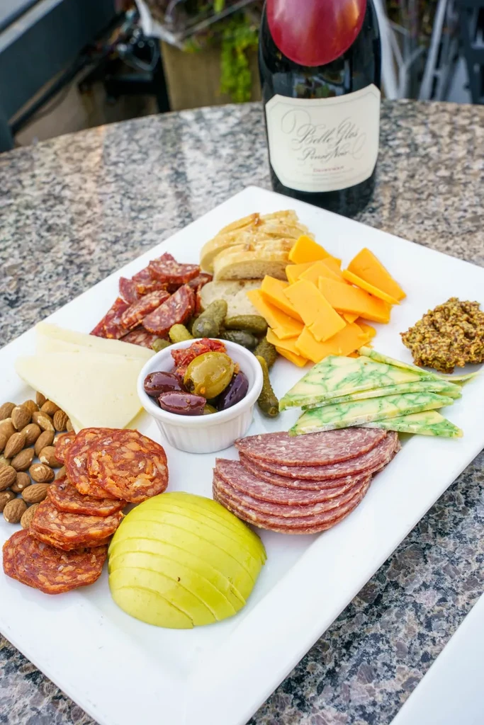 A charcuterie board with meats, cheeses, pickles, nuts, and apple slices.