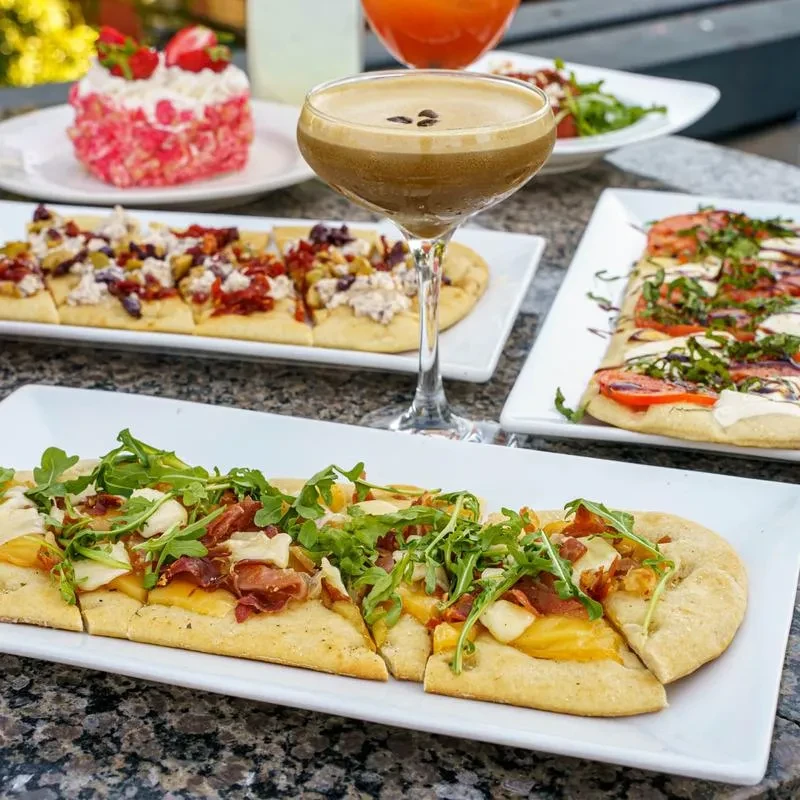 Multiple flatbreads, espresso martini, pink cake on a dark table.