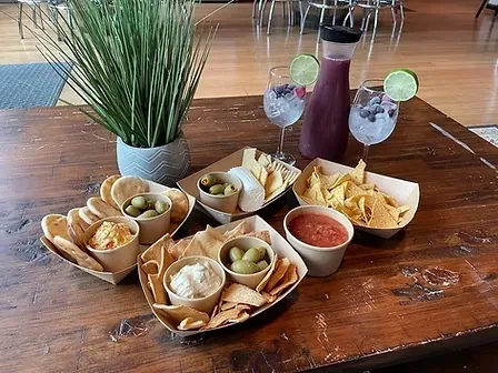 Hummus, chips, olives, cheese, and berry-lime drinks on a rustic table.