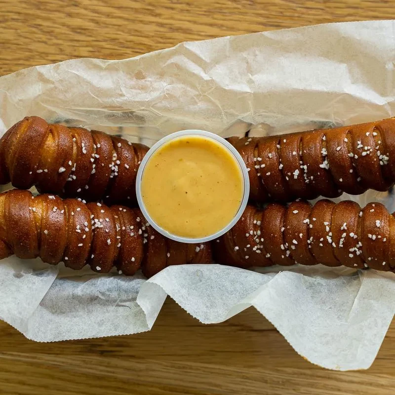 Basket with two braided, salted pretzels and creamy cheese dip.