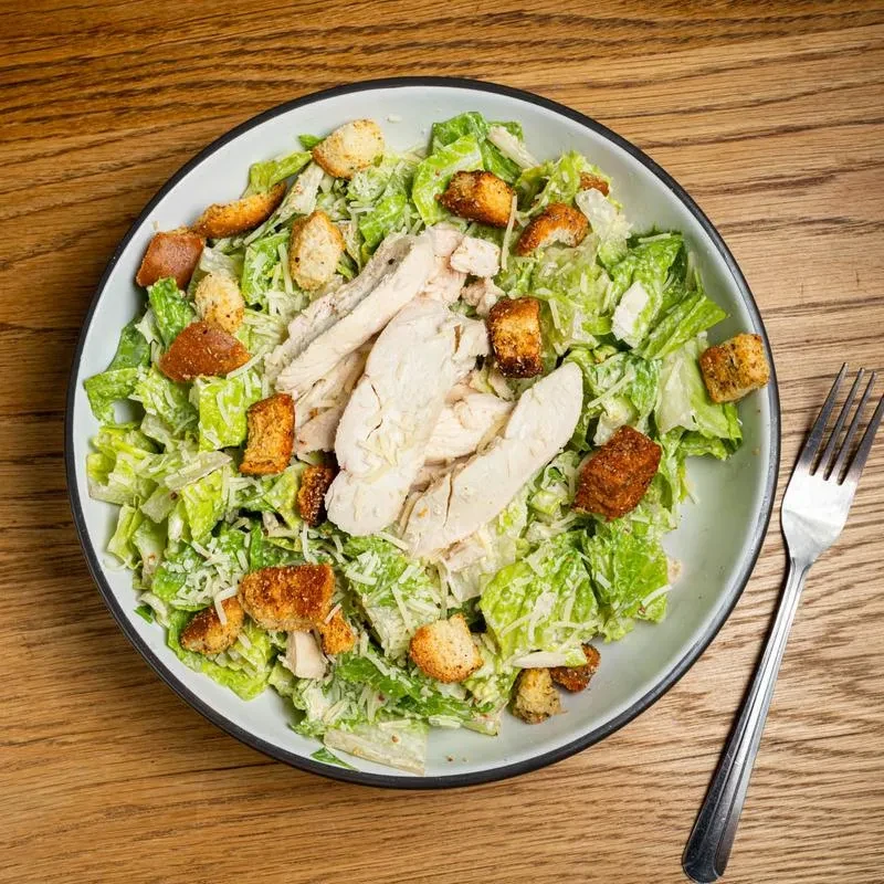 Overhead Caesar salad with grilled chicken, croutons, and Parmesan.
