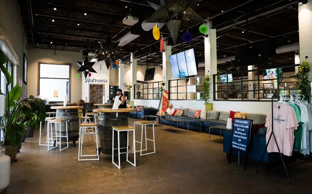 Industrial-chic restaurant interior with barrel tables, blue sofas, and exposed ductwork.