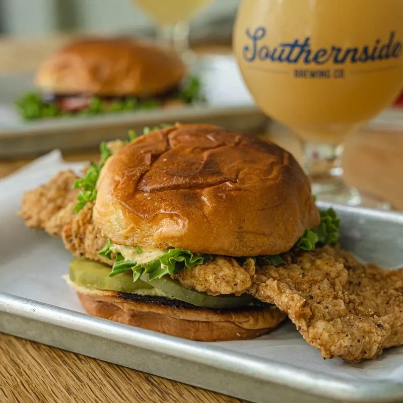 Crispy fried chicken sandwich with lettuce, pickles, and Southernsude Brewing beer.