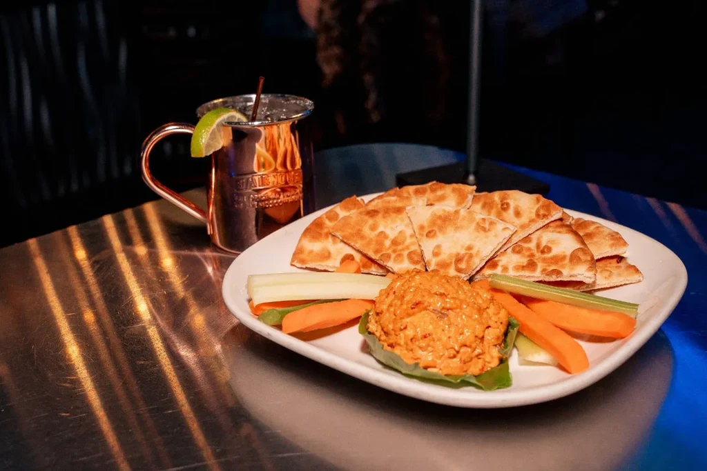 Close-up: orange dip, vegetables, pita, and a copper Moscow Mule.