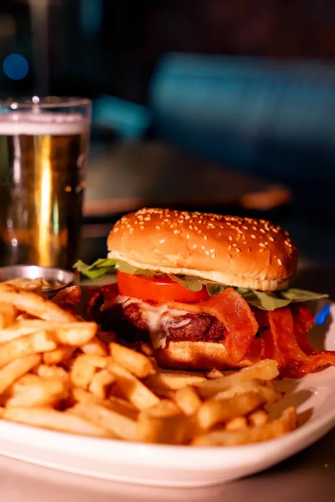 Burger with bacon, cheese, lettuce, tomato, fries, and beer.