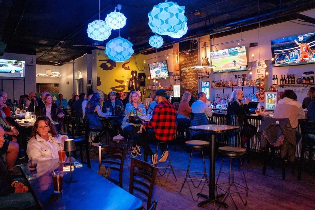 Modern bar interior with patrons, TVs, and spherical blue lights.
