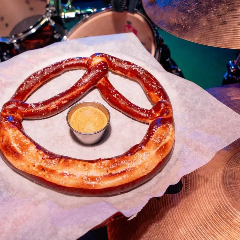Warm pretzel, coarse salt, mustard, and drum set at a bar.