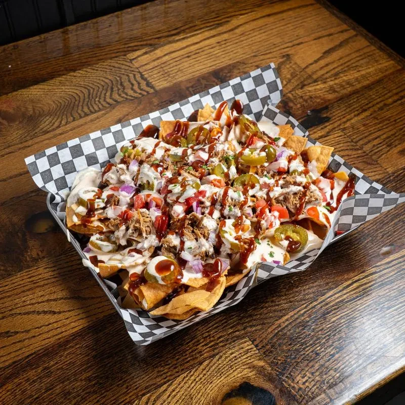 Large metal tray of loaded nachos with meat, sauces, and vegetables.