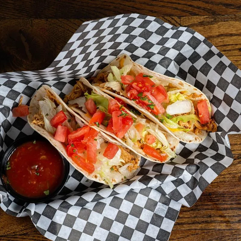 Three soft-shell tacos with shredded meat, lettuce, tomatoes, herbs, and salsa.