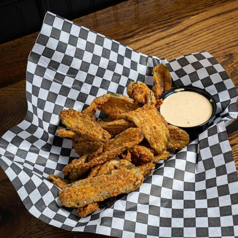 Fried vegetables in a basket on checkered paper with dipping sauce.