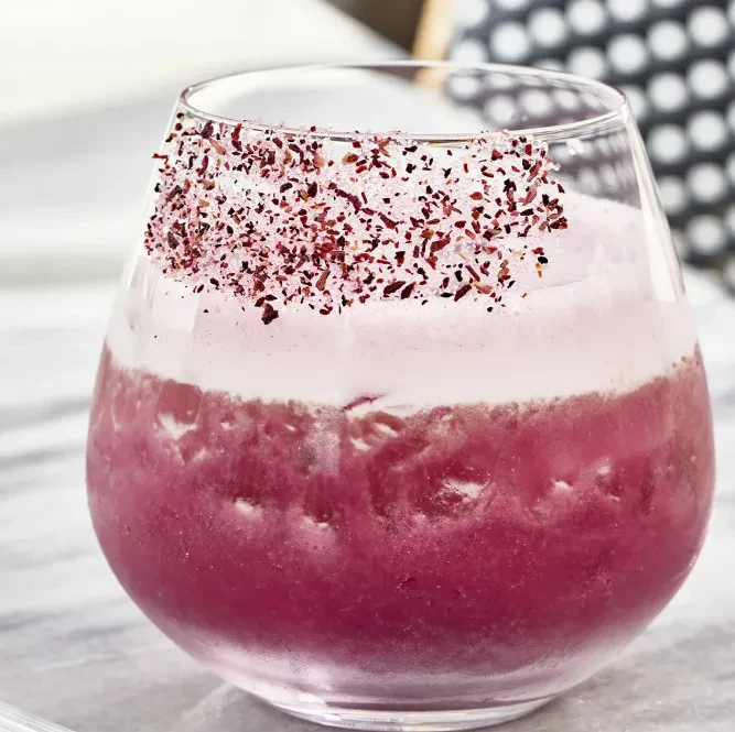 Frothy pink and magenta layered drink with a garnished rim.