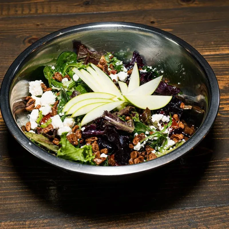 Salad in silver bowl with mixed greens, cheese, nuts, fanned apple.