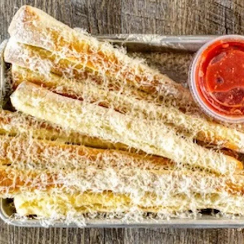 Cheesy breadsticks in a metal tray with marinara sauce on a wooden table.