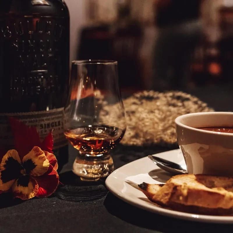 Whiskey glass, bottle, colorful flower, soup, and bread.