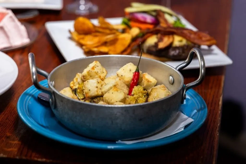 Metal pot with fried food, vegetables, and a red chili.