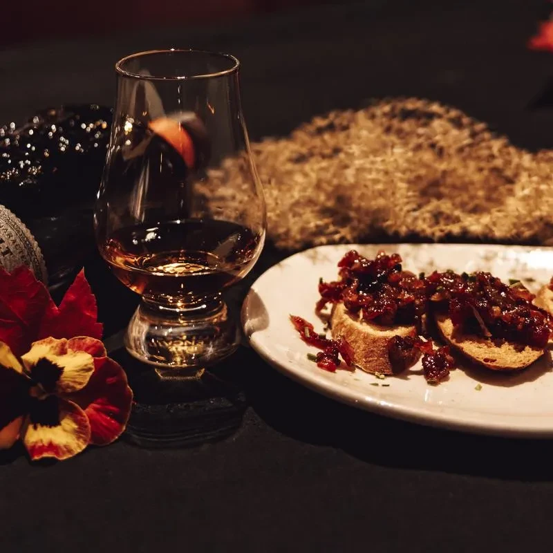 Amber spirit in Glencairn glass, bruschetta with relish, elegant setting.